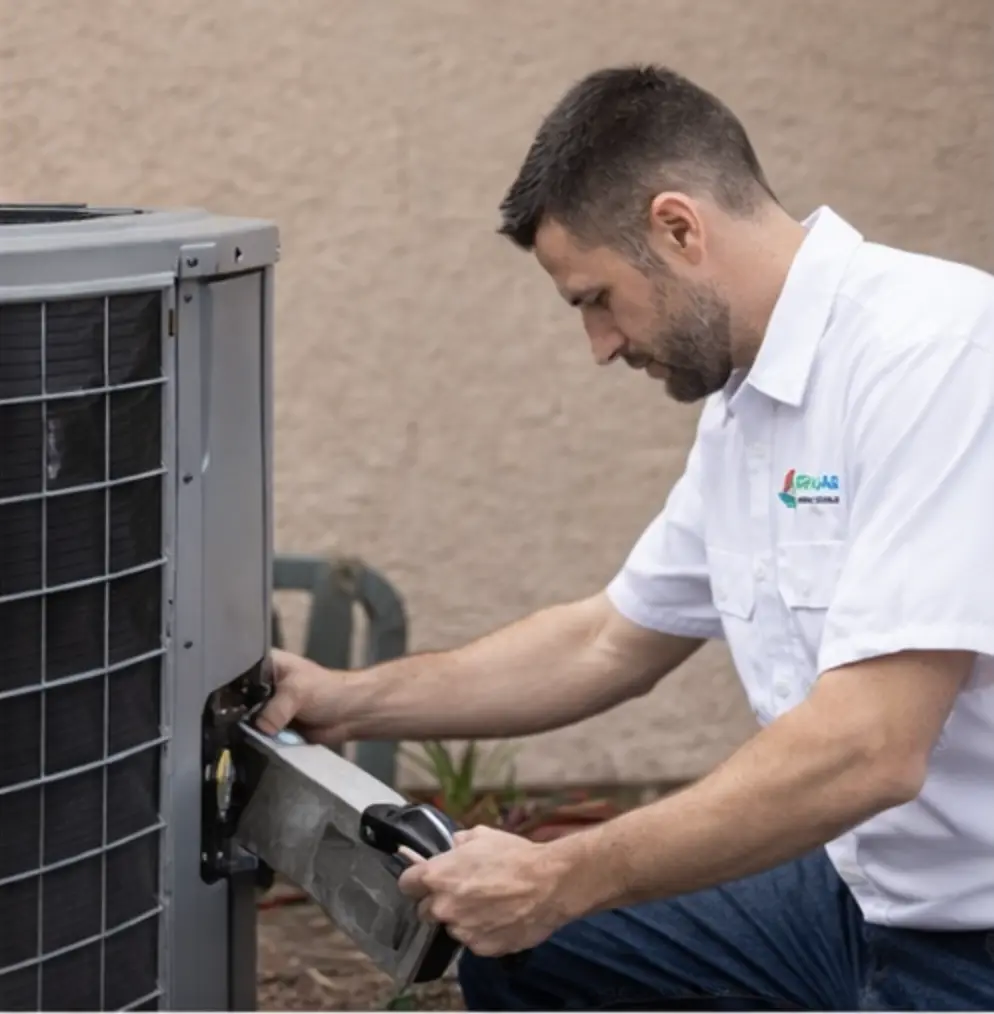 Green Air technician inspecting and cleaning outdoor AC condenser coils as part of a professional tune-up service